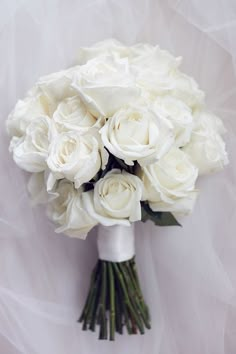 a bouquet of white roses sitting on top of a white cloth covered tablecloth with tulle