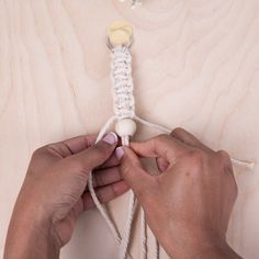 two hands are working on a piece of white string with a ball of yarn attached to it