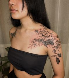 a woman wearing a black top with flowers on her chest and arm tattoo design in front of her left shoulder