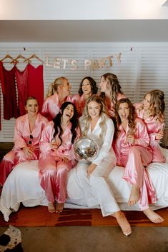 a group of women in pink robes sitting on a bed with one holding a silver ball