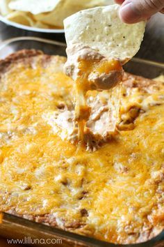 a hand dipping a tortilla chip into a casserole dish with cheese