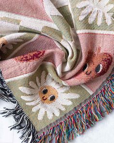 a multicolored scarf with fringes and flowers on it, laying on a white surface