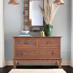 a wooden dresser sitting under a mirror next to a lamp and a vase on top of it