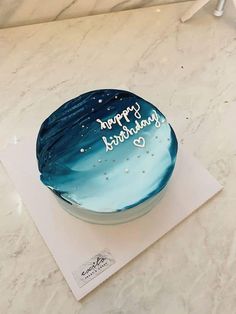 a blue and white birthday cake sitting on top of a marble countertop covered in frosting