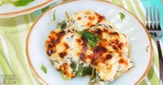 a white plate topped with lasagna covered in cheese and spinach next to a fork