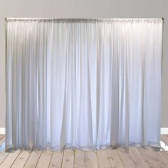 an empty room with white curtains and wooden floors in front of the wall that is partially closed