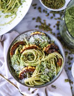 a bowl filled with pasta and pesto on top of a white cloth next to two bowls