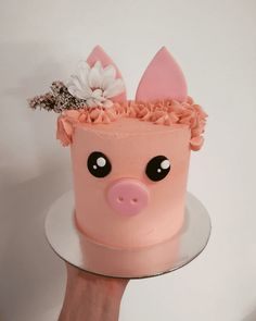 a hand holding a pink cake decorated like a pig with flowers on it's head