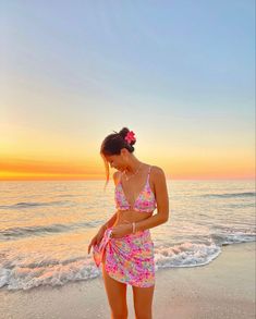 a woman standing on top of a sandy beach next to the ocean wearing a bathing suit