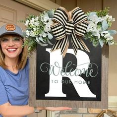 a woman holding up a sign that says welcome to our home with a bow on it