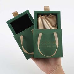 a hand holding up a green box with gold ribbon and the inside of it is empty