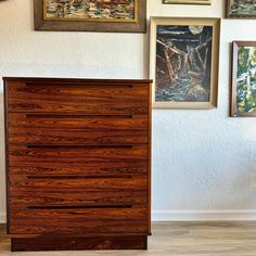 a wooden dresser sitting next to a wall with pictures on it