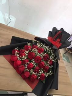 a bouquet of red roses is wrapped in black paper and sits on a wooden table