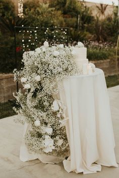 a table topped with a cake and flowers next to a white cloth covered tablecloth