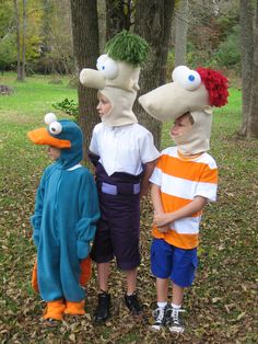 three children in costume standing next to each other near trees and grass with heads on their heads