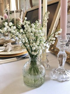 white flowers in a glass vase on a table with candles and other decorations behind it