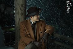 a man in a brown coat and hat sitting on a porch