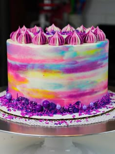 a multicolored cake sitting on top of a silver platter covered in purple and pink frosting