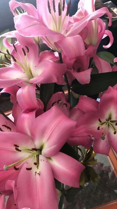 pink lilies are in a vase on a table with other flowers and greenery