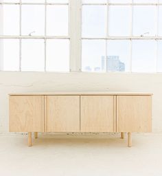 a wooden cabinet sitting in front of a window next to a white wall with two windows