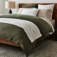 the bed is made with green comforter and pillows on top of carpeted flooring