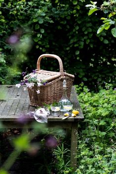 a picnic table in the middle of a garden with flowers on it and a wicker basket