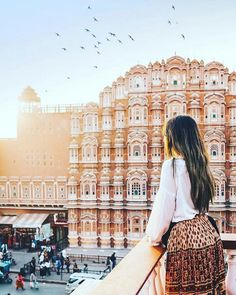 a woman looking out over the city with birds flying in the air above her head