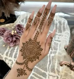 a woman's hand with henna tattoos on it and flowers in the background