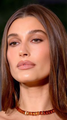 a woman with long hair wearing an orange necklace and brown eyeshadow is looking off to the side