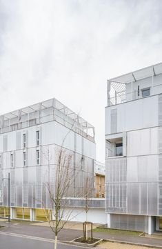 two large white buildings next to each other on the side of a road with trees in front of them