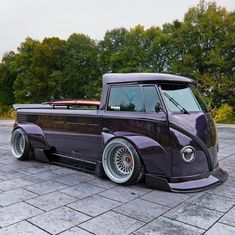 an old purple truck parked on top of a parking lot with trees in the background