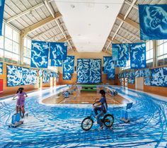 two children riding bikes in an indoor swimming pool with artwork on the walls and ceiling