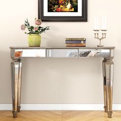 a painting on the wall above a console table with vases and flowers in it