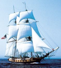 a large white sail boat sailing in the ocean with an american flag on it's mast