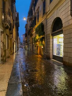 an empty city street at night with rain on the ground and buildings lining both sides