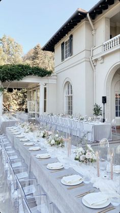 a long table is set with white plates and silverware for an outdoor wedding reception