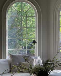 a living room filled with white furniture and large arched windows above the couch is a vase full of flowers