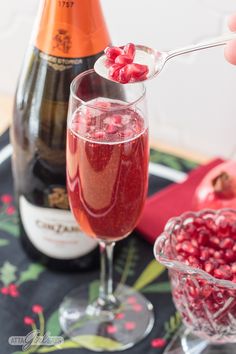 a glass filled with liquid next to a bottle of wine and a bowl of pomegranates