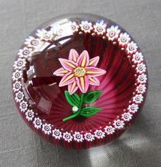 a red glass bowl with a flower painted on the side and green leaves sticking out of it