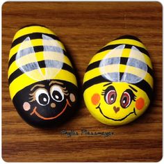 two painted rocks sitting on top of a wooden table covered in black and yellow stripes