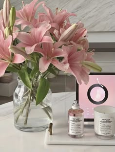 a vase filled with pink flowers on top of a white table next to a laptop