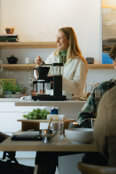 a woman standing in front of a blender on top of a counter next to two men