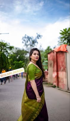 a woman in a green and purple sari standing on the side of a road