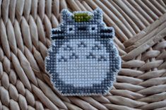 a cross stitch totoro brooch sitting on top of a wicker basket