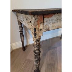 an old wooden table sitting on top of a hard wood floor next to a wall