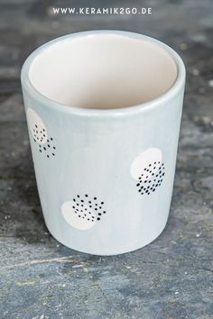 a white cup sitting on top of a stone floor next to a planter with holes in it