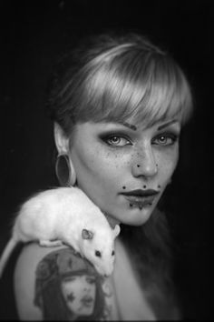 a woman with black makeup holding a white rat on her shoulder and looking at the camera