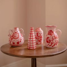 three red and white vases sitting on top of a wooden table