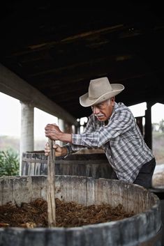 a man wearing a cowboy hat leaning over a barrel filled with dirt and mulch