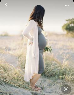 a pregnant woman standing in the sand at the beach